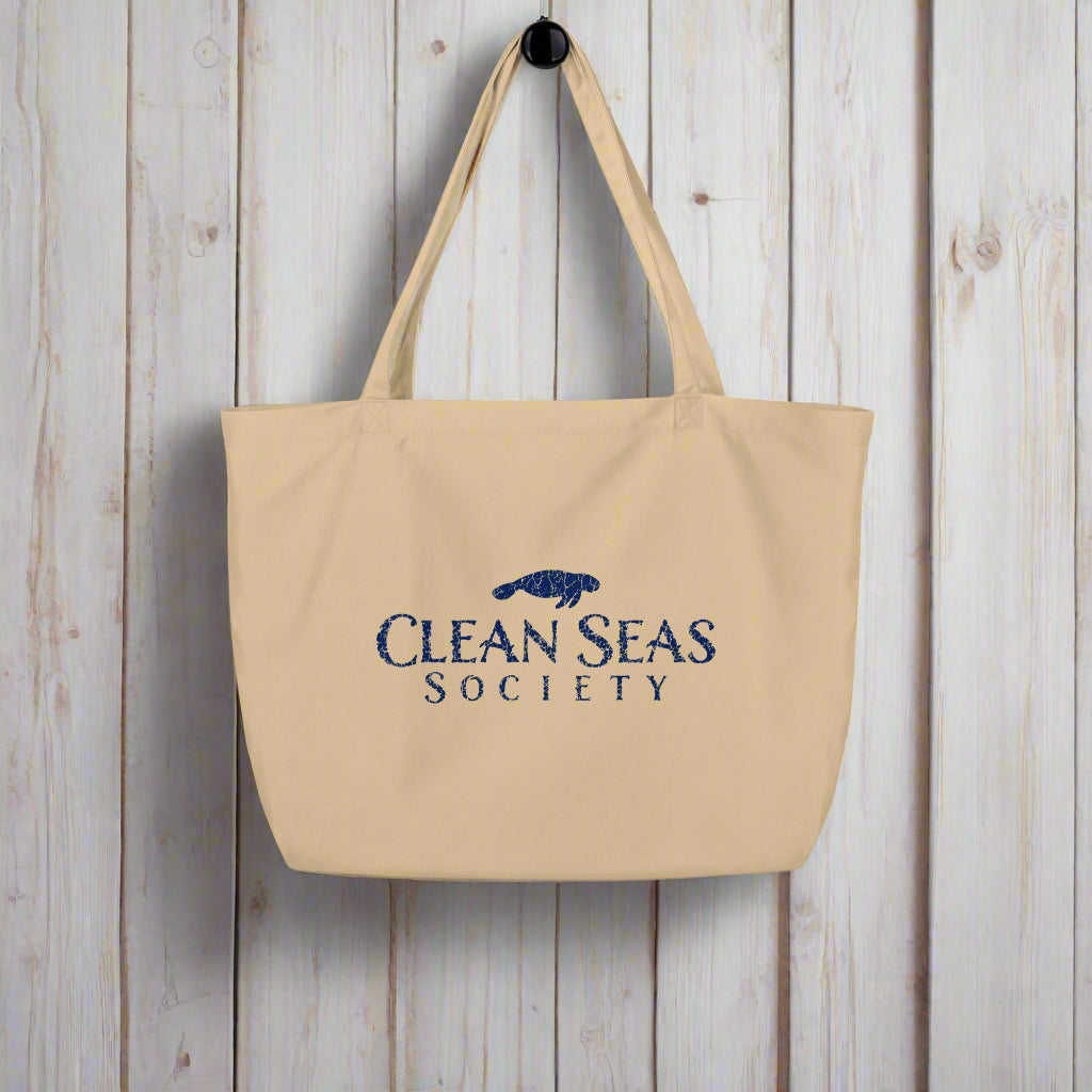 Large organic tote bag from Clean Seas Society hanging on a rustic nautical wood wall