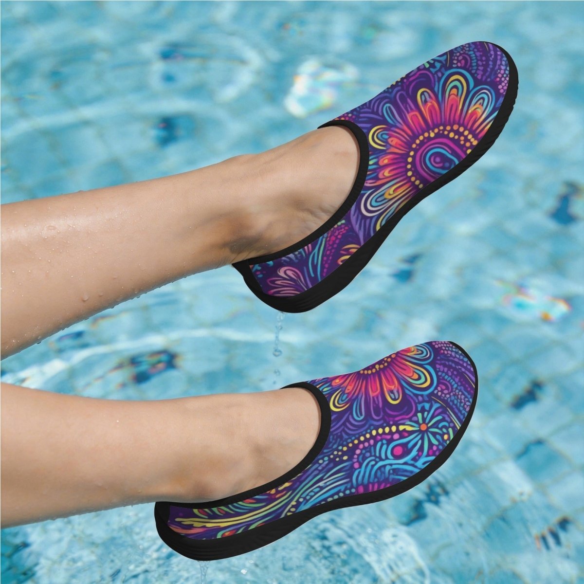 A pair of slip-on water shoes with a vibrant multicolor tribal pattern in purple, blue, pink, and orange, shown on a person's feet in a swimming pool.