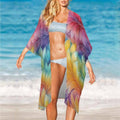 Woman on a beach wearing a colorful kimono-style long cover up with a blue ocean background