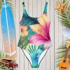 Tropical floral print one-piece swimsuit surrounded by beach items like a surfboard, starfish, and ukulele.