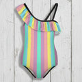 Girls Striped swimsuit with tropical colors and ruffles and adjustable black strap floating over a rustic wood background.
