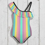 Girls Striped swimsuit with tropical colors and ruffles and adjustable black strap floating over a rustic wood background.