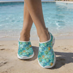 A person standing on a sandy beach near a swimming pool wearing slip-on water shoes with a Baby Sea Turtles pattern.