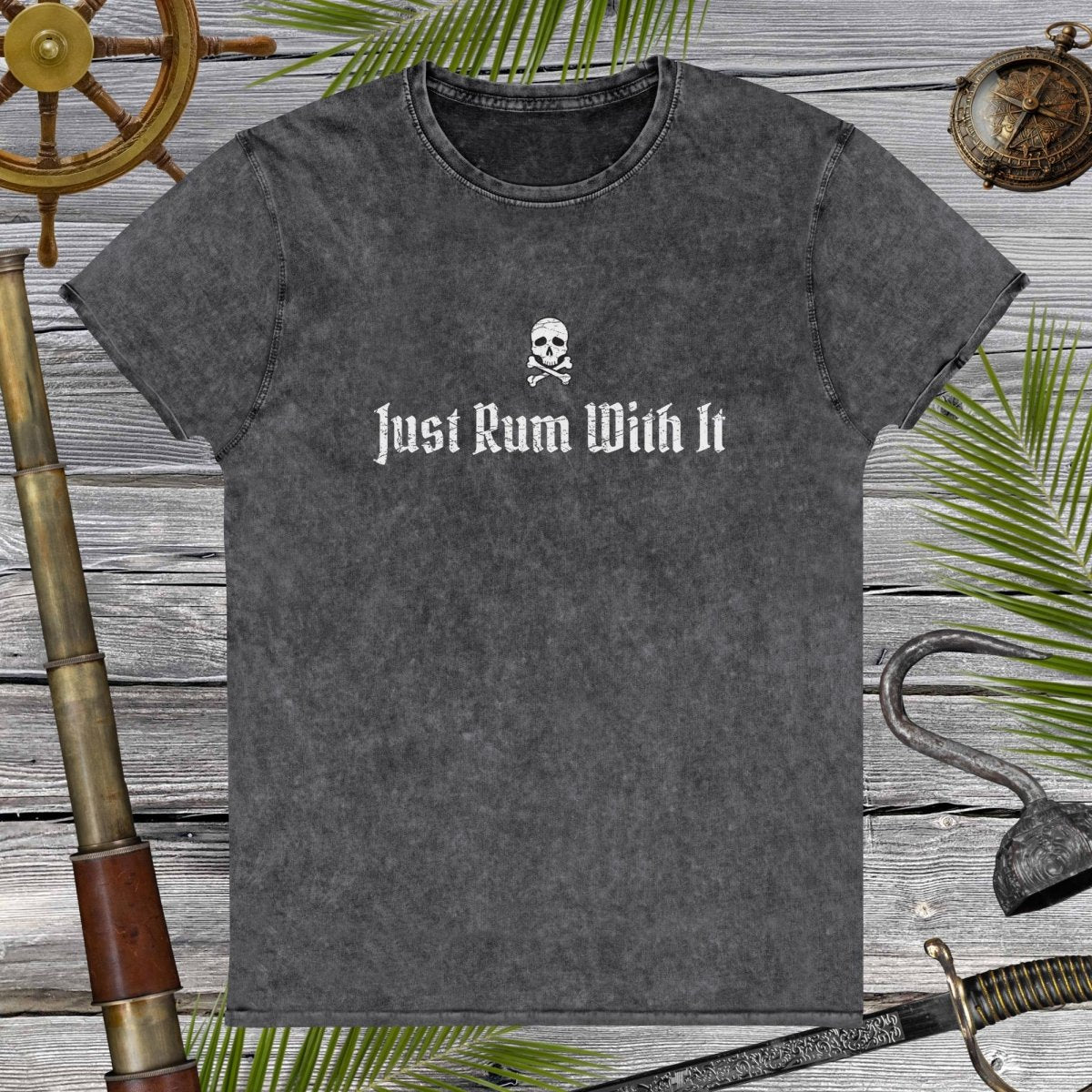 Gray t-shirt with skull and crossbones design and text 'Just Rum With It' on a wooden background with nautical items.