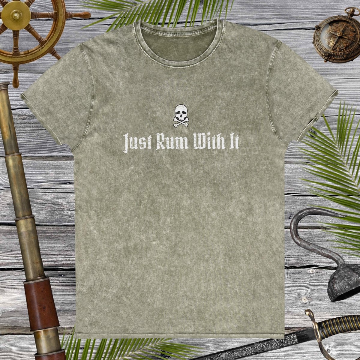 Green t-shirt with skull and crossbones design and text 'Just Rum With It' on a wooden background with nautical items.