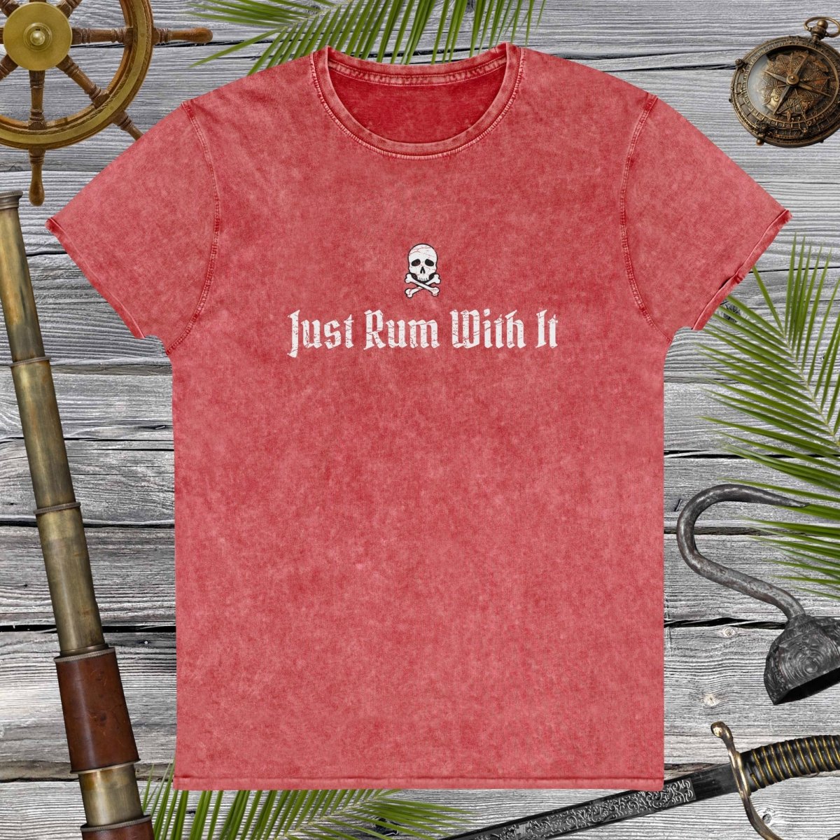 Red t-shirt with 'Just Rum With It' text and skull design on a wooden background with nautical items.