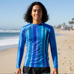 A teenage dude standing on Venice Beach wearing a long-sleeve blue striped rash guard and black swim trunks.