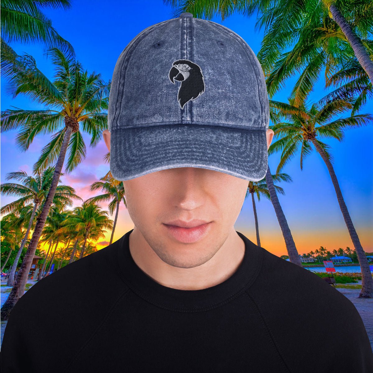 Person wearing a denim Parrot Head Hat with a logo against a tropical sunset background