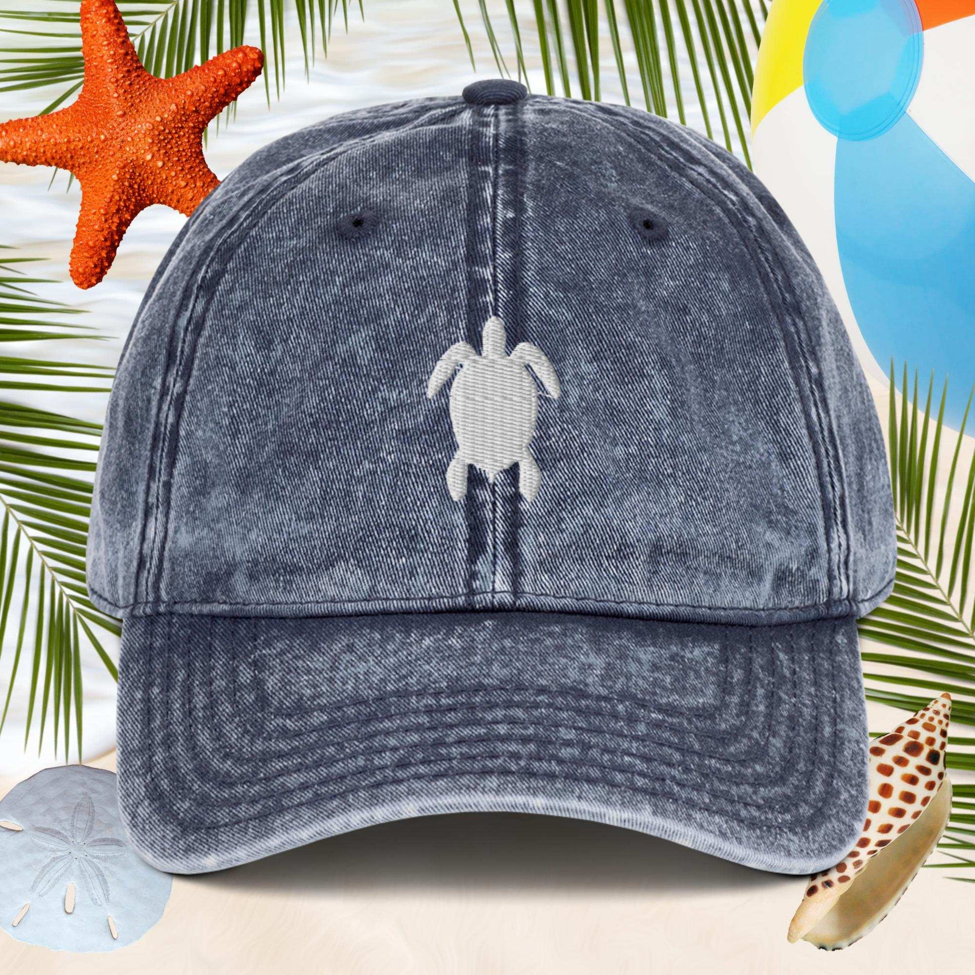 Blue denim cap with turtle emblem on a beach-themed background