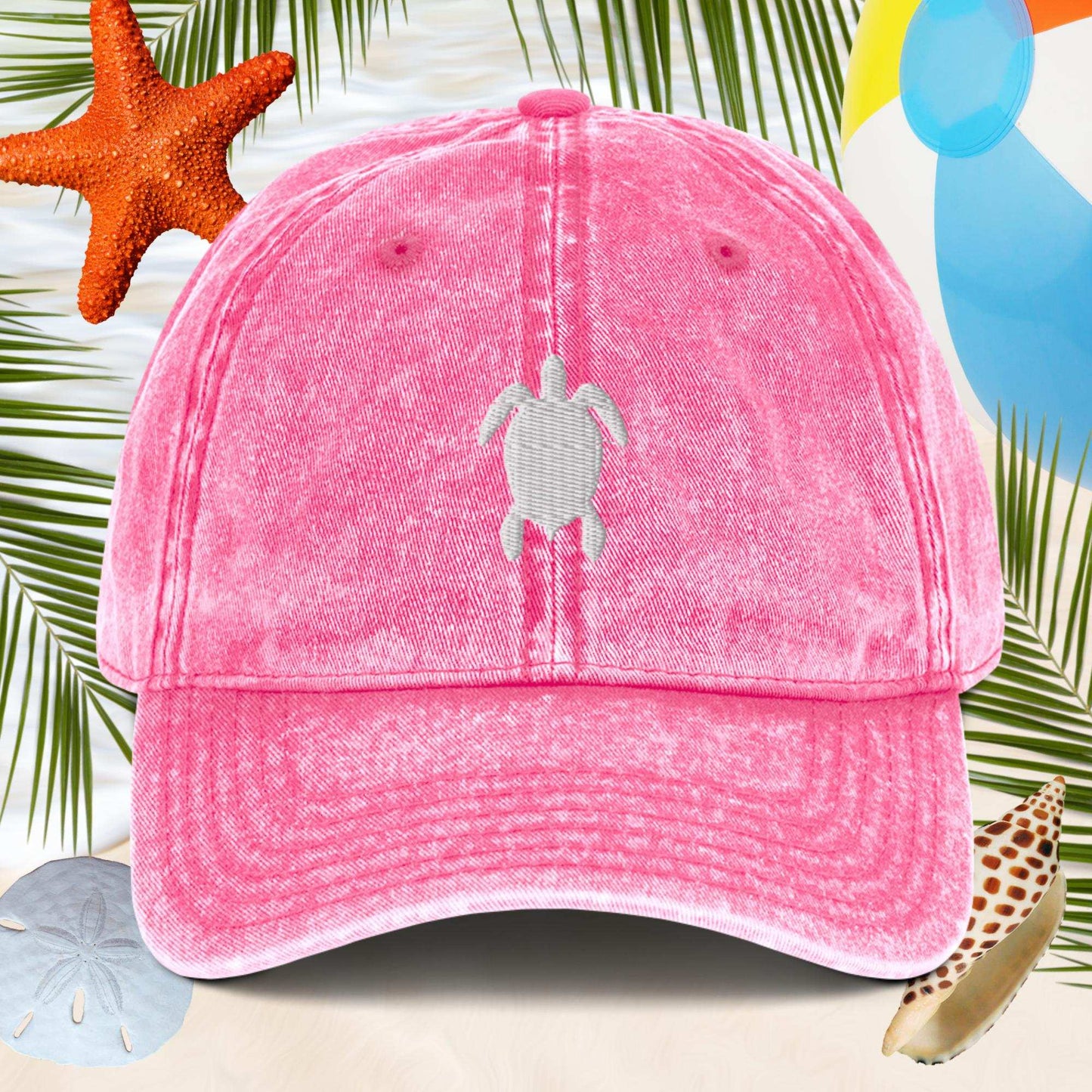 Pink cap with a turtle design on a beach-themed background with starfish and sand dollars.