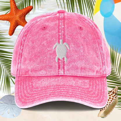 Pink cap with a turtle design on a beach-themed background with starfish and sand dollars.