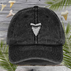 Black cap with a white Embroidered Shark Tooth on a wooden background with shark fins and palm leaves.