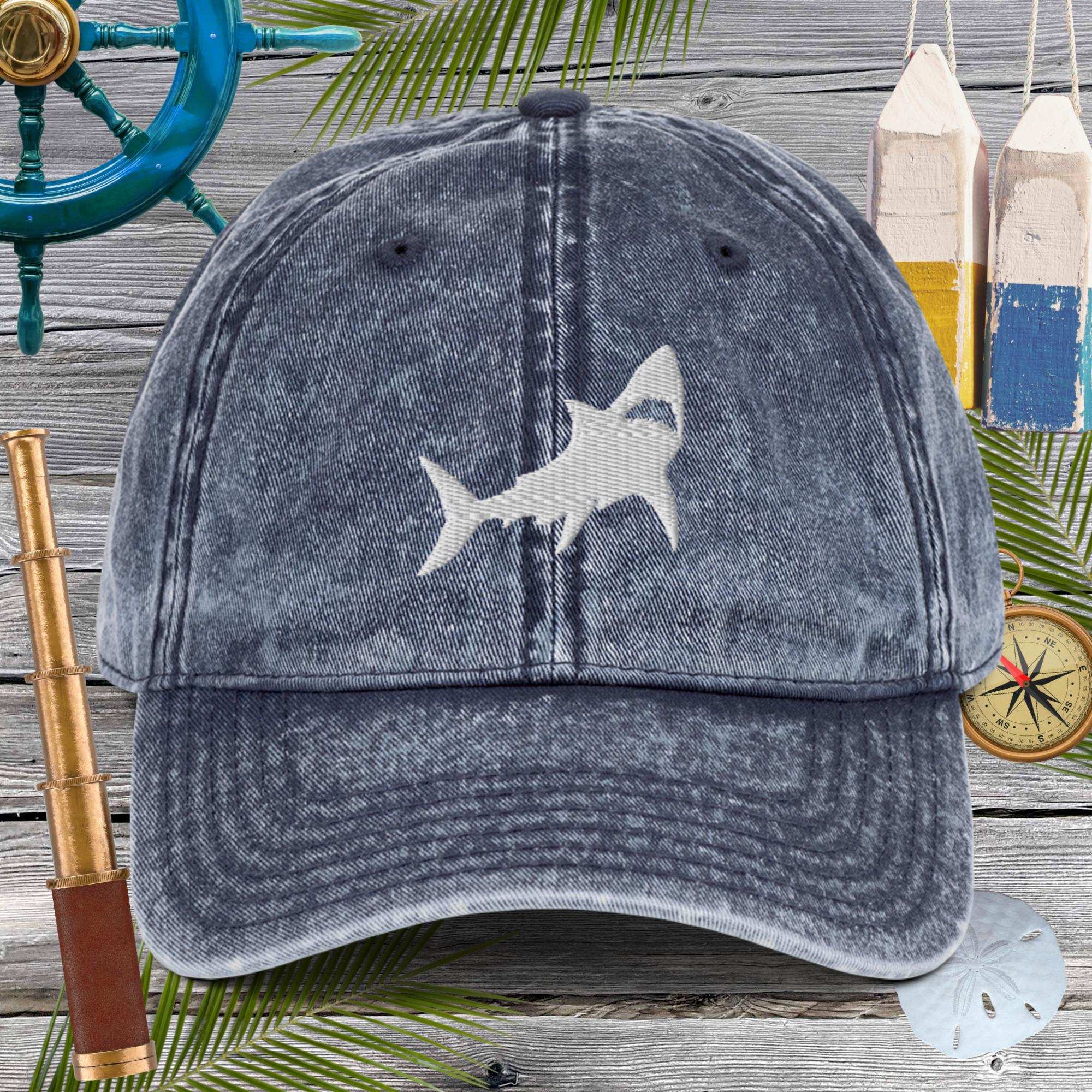 Blue denim cap with embroidered shark design on a nautical-themed background