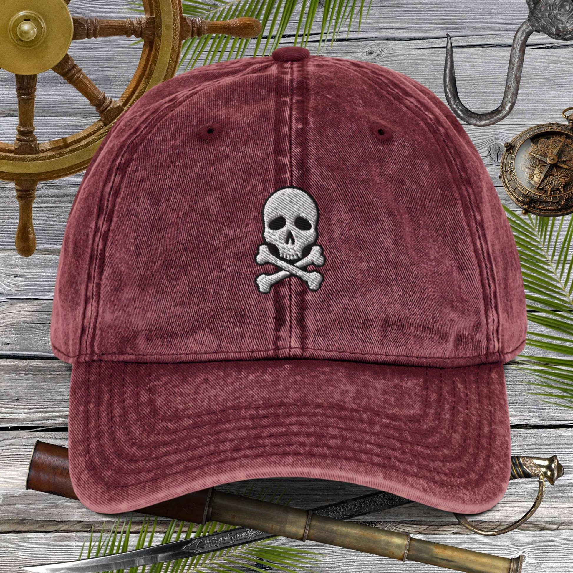 Skull And Crossbones Vintage Cotton Twill Cap displayed against nautical themed background with ship wheel and tools.