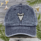 Blue denim cap with Embroidered Shark Tooth design on a wooden background with shark teeth and palm leaves.