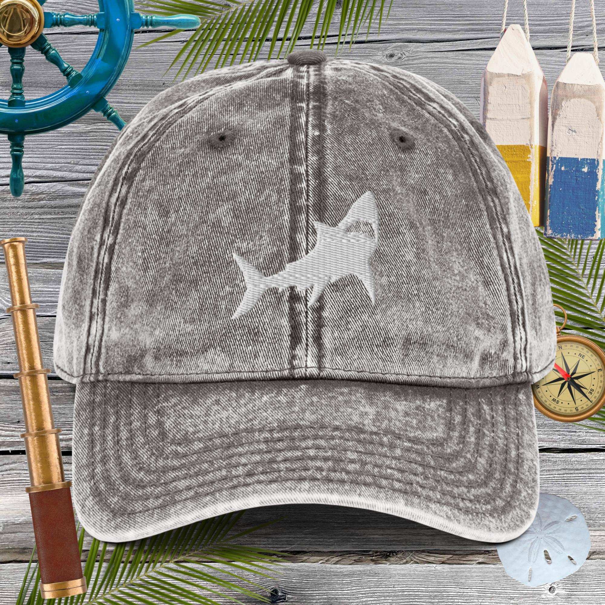 Gray cap with a shark design on a wooden background with nautical items.