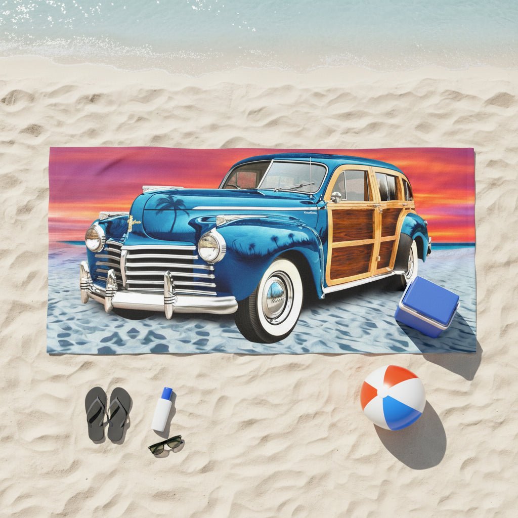 A rectangular beach towel featuring a vintage blue wood-paneled station wagon on a sandy beach under a colorful sunset sky.