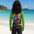 A person standing on a sandy beach in virgin islands with turquoise water and islands in the background, viewed from behind. The person is wearing a long-sleeve green rash guard with a large, colorful parrot graphic printed across the back.