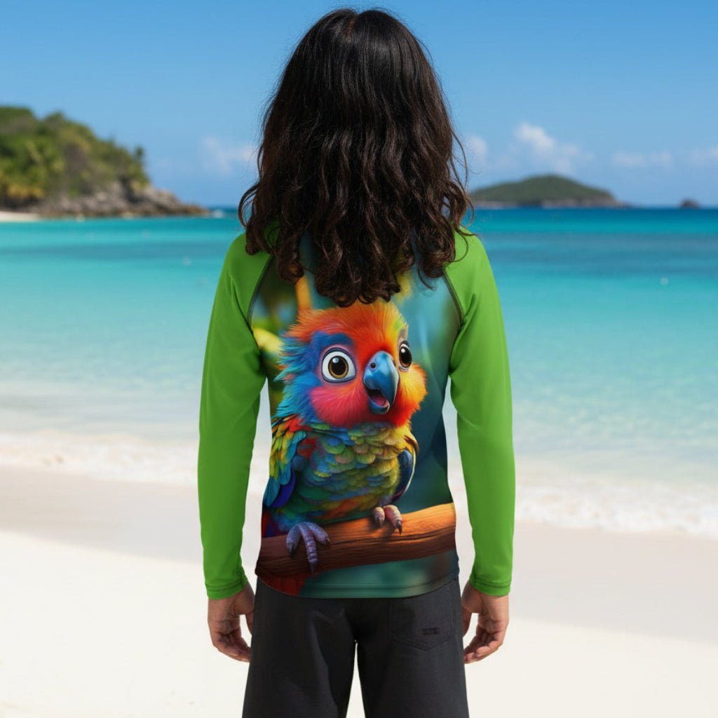 A person standing on a sandy beach in virgin islands with turquoise water and islands in the background, viewed from behind. The person is wearing a long-sleeve green rash guard with a large, colorful parrot graphic printed across the back.