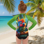 A child shown from behind wearing a long-sleeve rash guard with a colorful parrot graphic on the back, standing on a sandy beach with palm trees and turquoise water in the background.