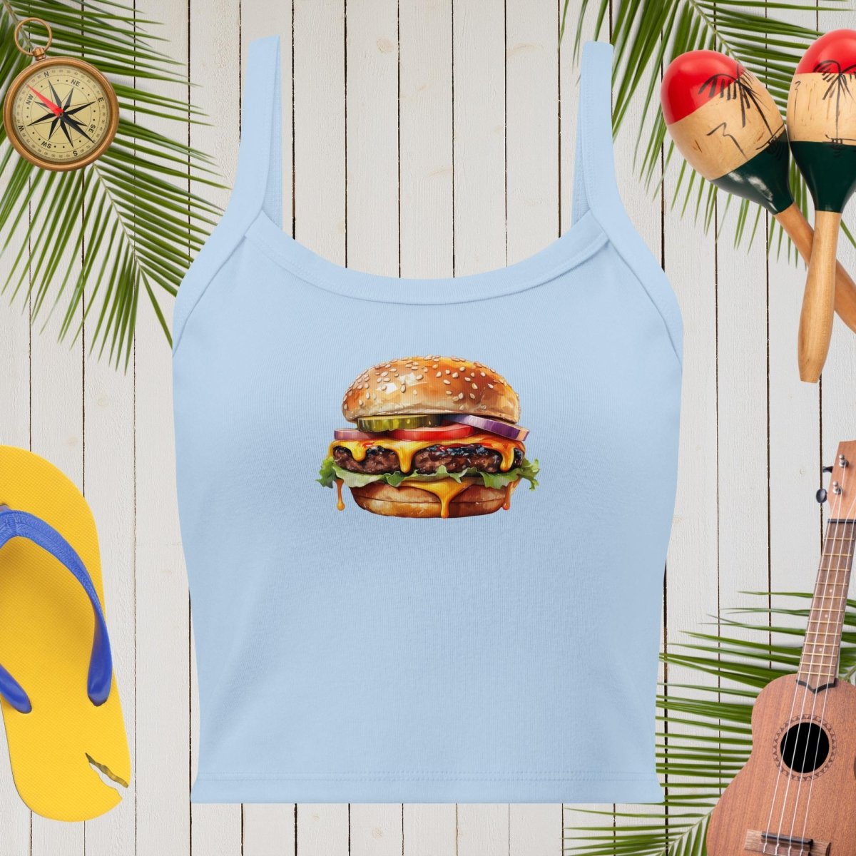 Light blue tank top with a hamburger graphic on a wooden background with tropical elements.