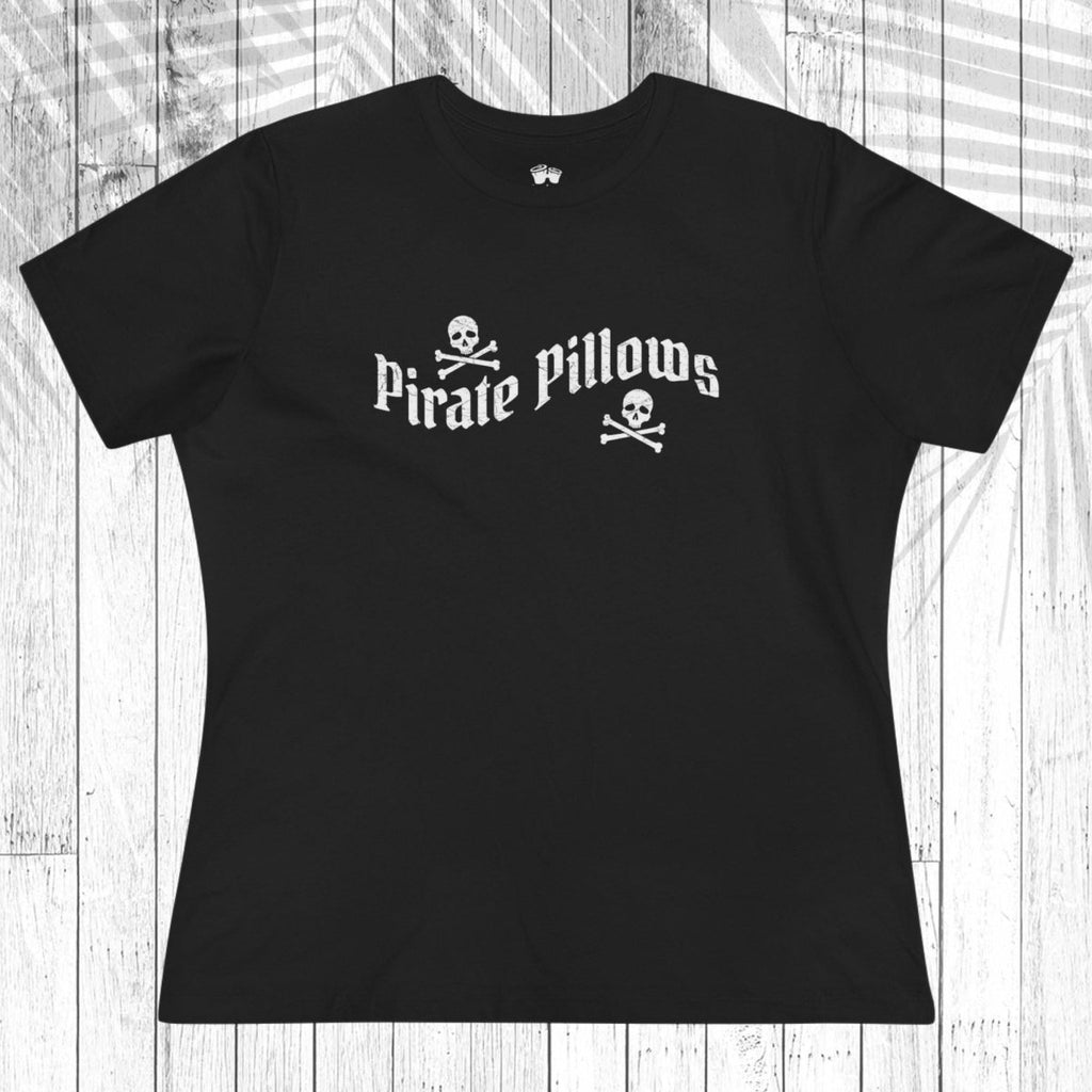 A navy blue short-sleeve t-shirt with a white graphic reading 'Pirate Pillows' and skull-and-crossbones icons, laid flat on a white wood plank background.