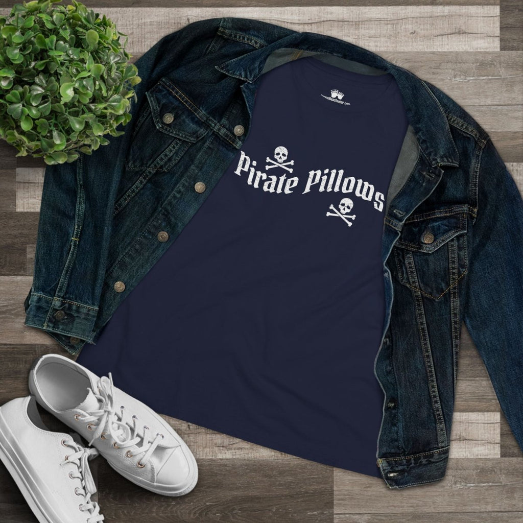 A navy blue graphic t-shirt with 'Pirate Pillows' and skull-and-crossbones text, styled in a flat lay with an open dark denim jacket, white sneakers, and a small green plant on a wood plank background.