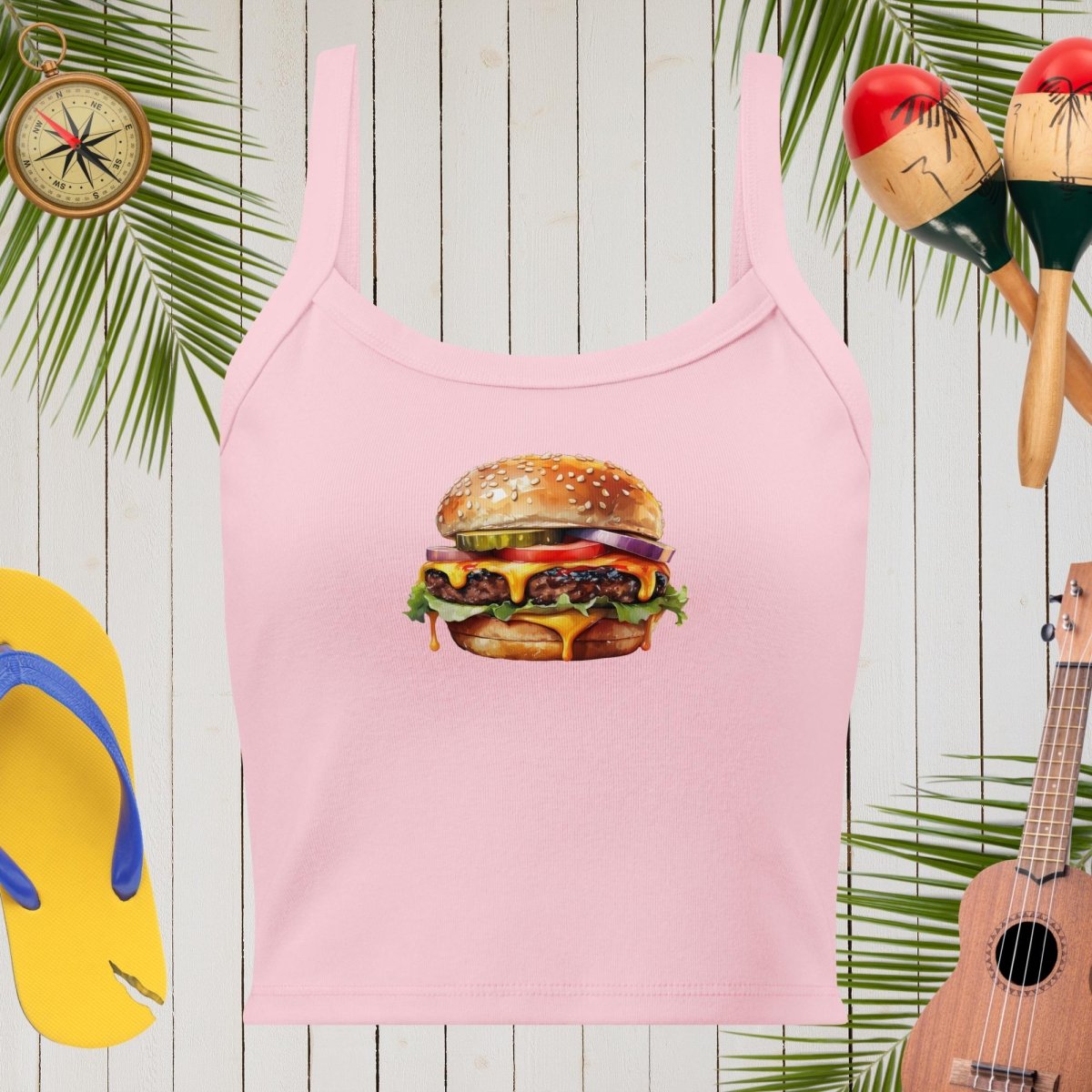 Pink tank top with a hamburger graphic on a wooden background with tropical elements.