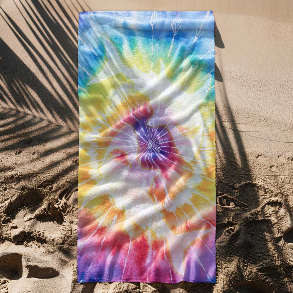 Sharks printed on a tie dye beach towel surrounded by beach sand an the shadow of a palm tree